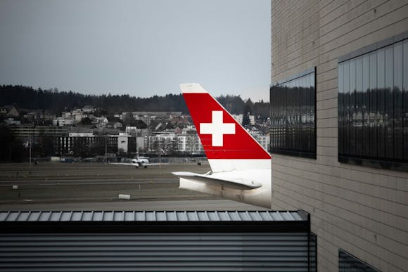 Tail of a Zurich plane with their flag, visible behind the airport building