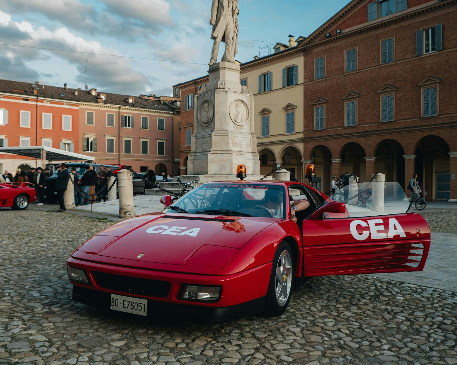 Ferrari d'epoca in primo piano, sullo sfondo piazza e edifici in centro a Modena  