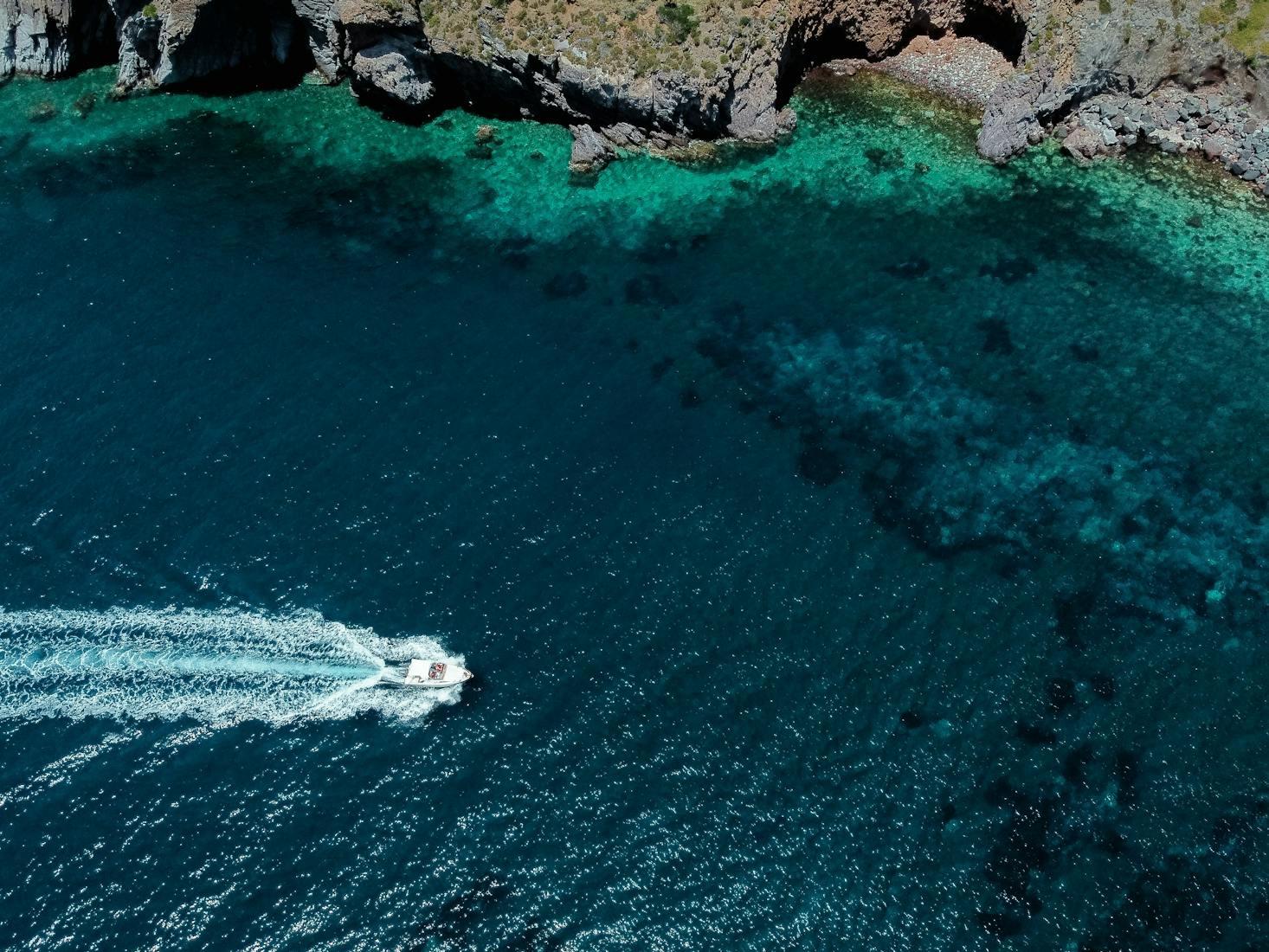 Splendido mare verde acqua di Lipari, con scogli e una barca con scia dietro di sé