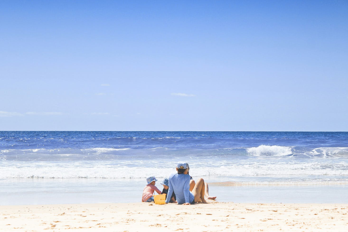 A family sitting by the water in the white sand on one of the beaches near Brisbane