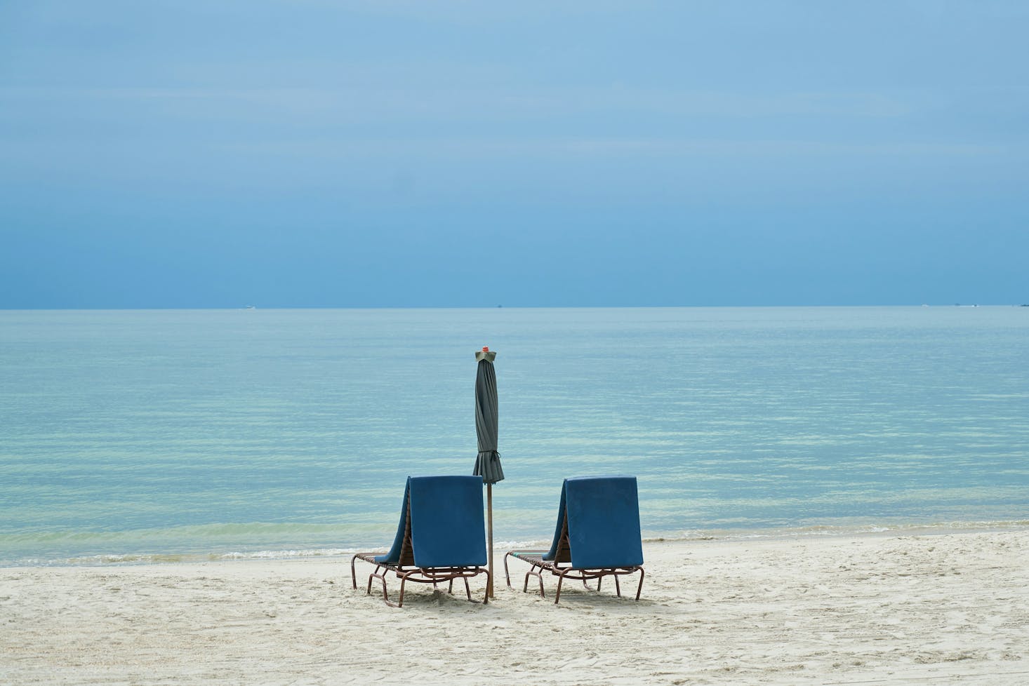 Two empty beach chairs and a closed umbrella on the white sand of Langkawi island 