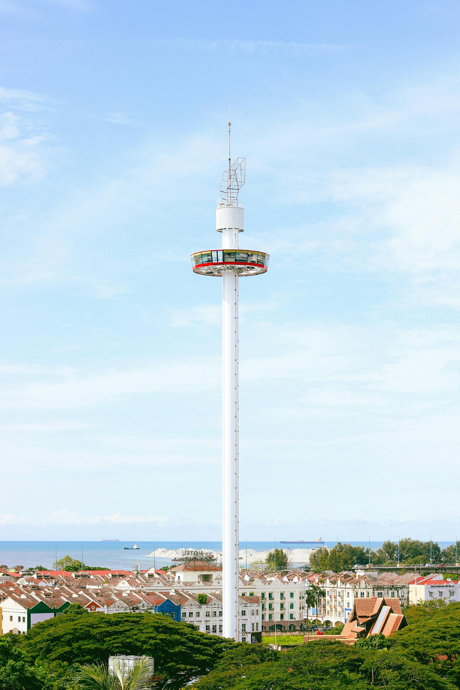 Tall, thin white tower and rooftops of Malacca with Klebang Beach in the distance