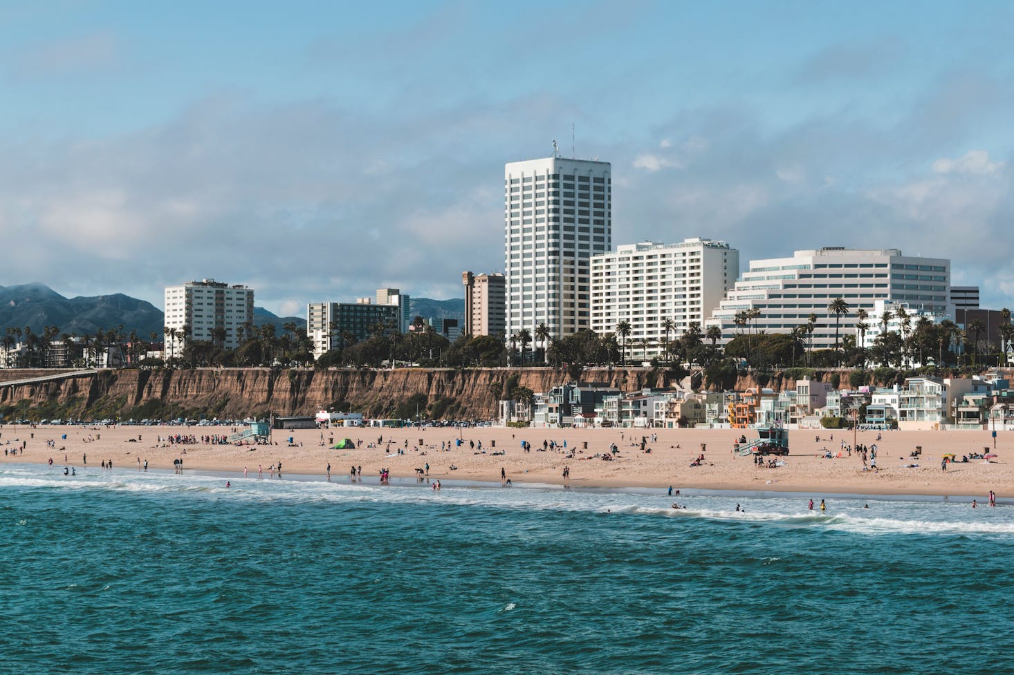 View back from Santa Monica Pier to the beach with large, white buildings in the distance