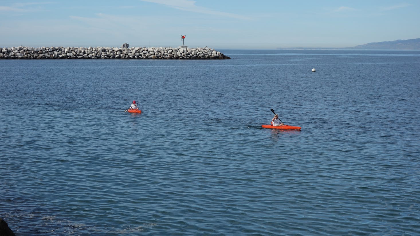 A person in a red kayak in the blue water of Playa del Rey