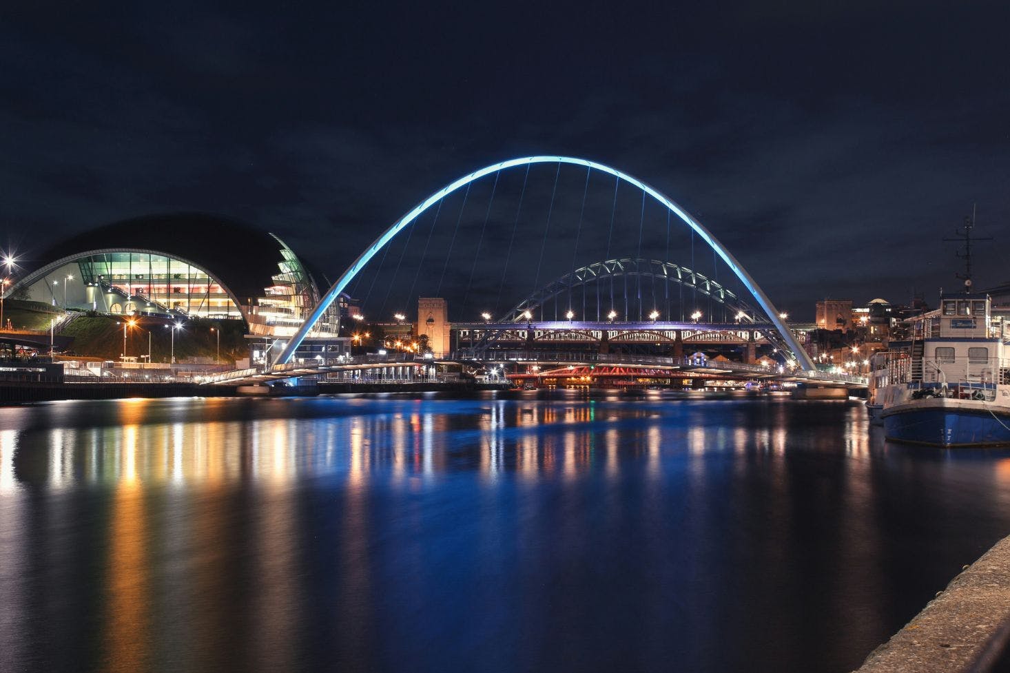 Gateshead Millennium Bridge over the Tyne, with a modern building, a boat, and the city in the background