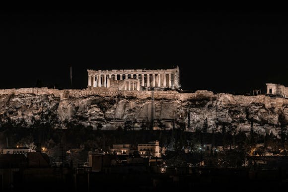 Lit up Parthenon on a hill in Athens with buildings below it at night