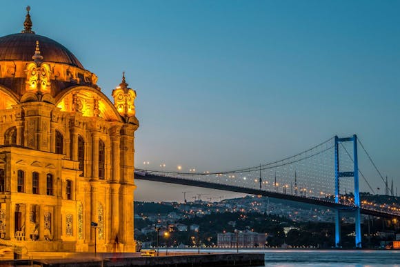 Ortaköy Mosque glowing at night, with the Bosphorus Bridge and city skyline visible after sunset