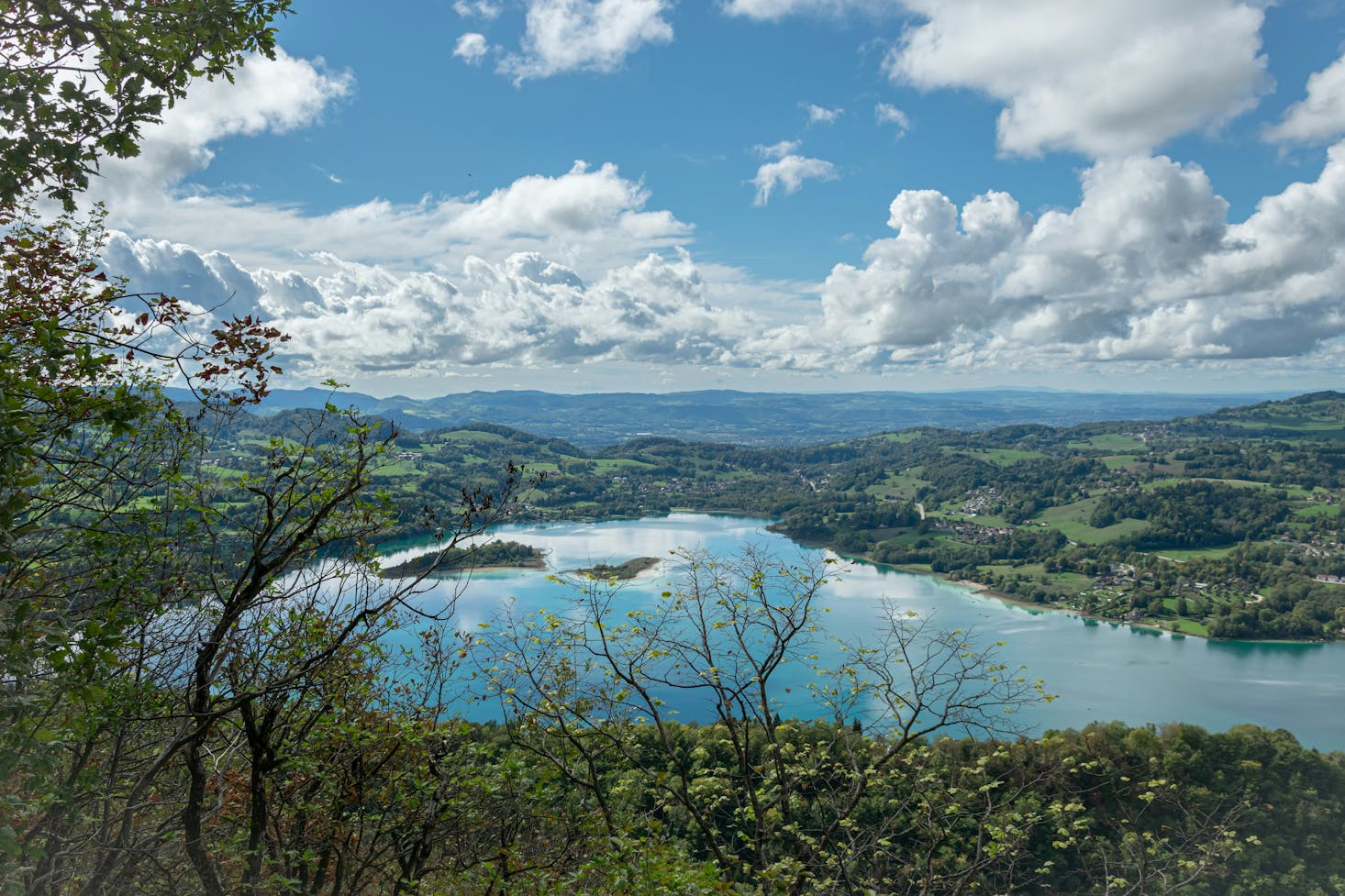 Aerial view of Lake Aiguebelette near Lyon with green hills and calm water reflecting blue sky and white clouds