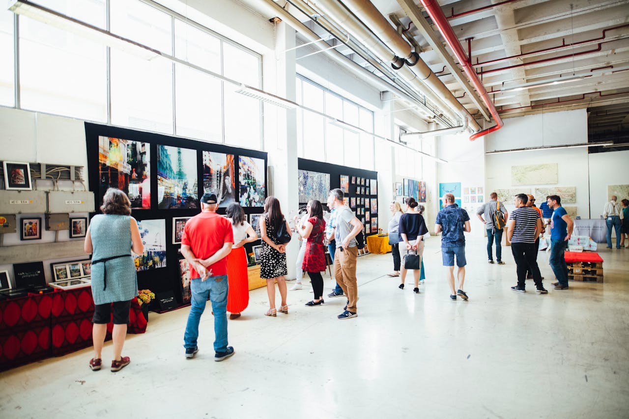 A crowd viewing beautiful artworks hung on several walls in an art market