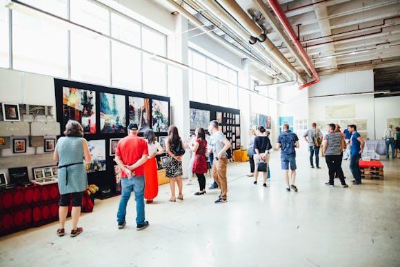 A crowd viewing beautiful artworks hung on several walls in an art market