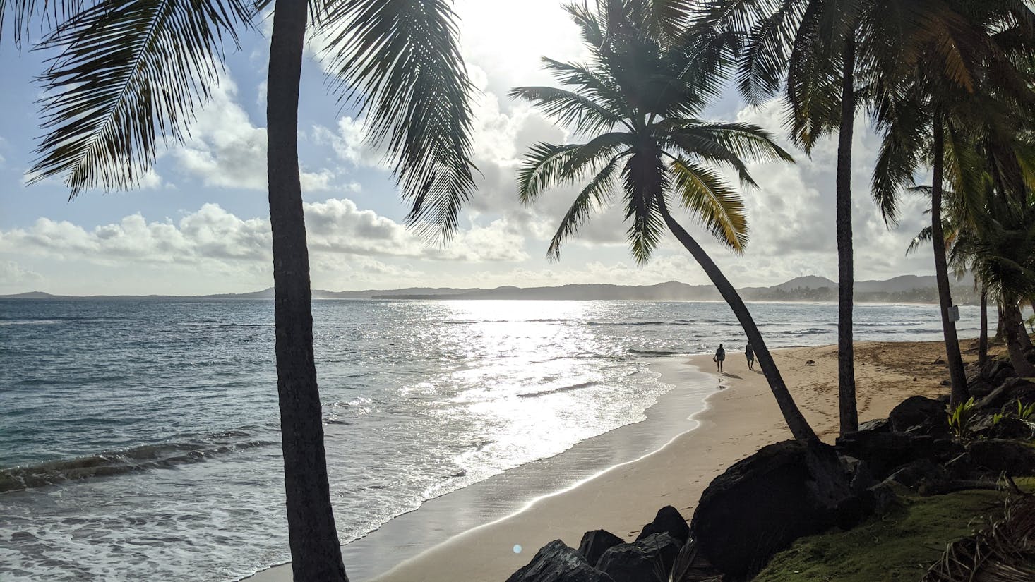 Gentle waves and palm trees with 2 people walking along the sand at Luquillo Beach near San Juan