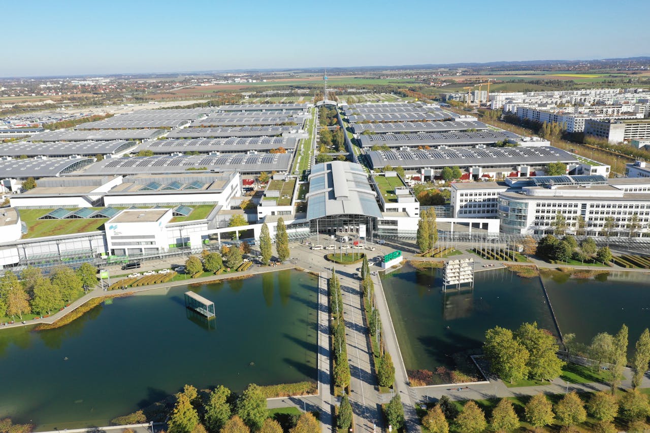 The vast white and grey Messe Munich building during daytime next to a body of water