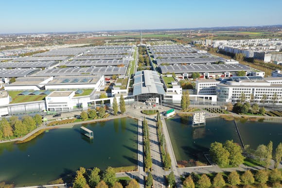 The vast white and grey Messe Munich building during daytime next to a body of water