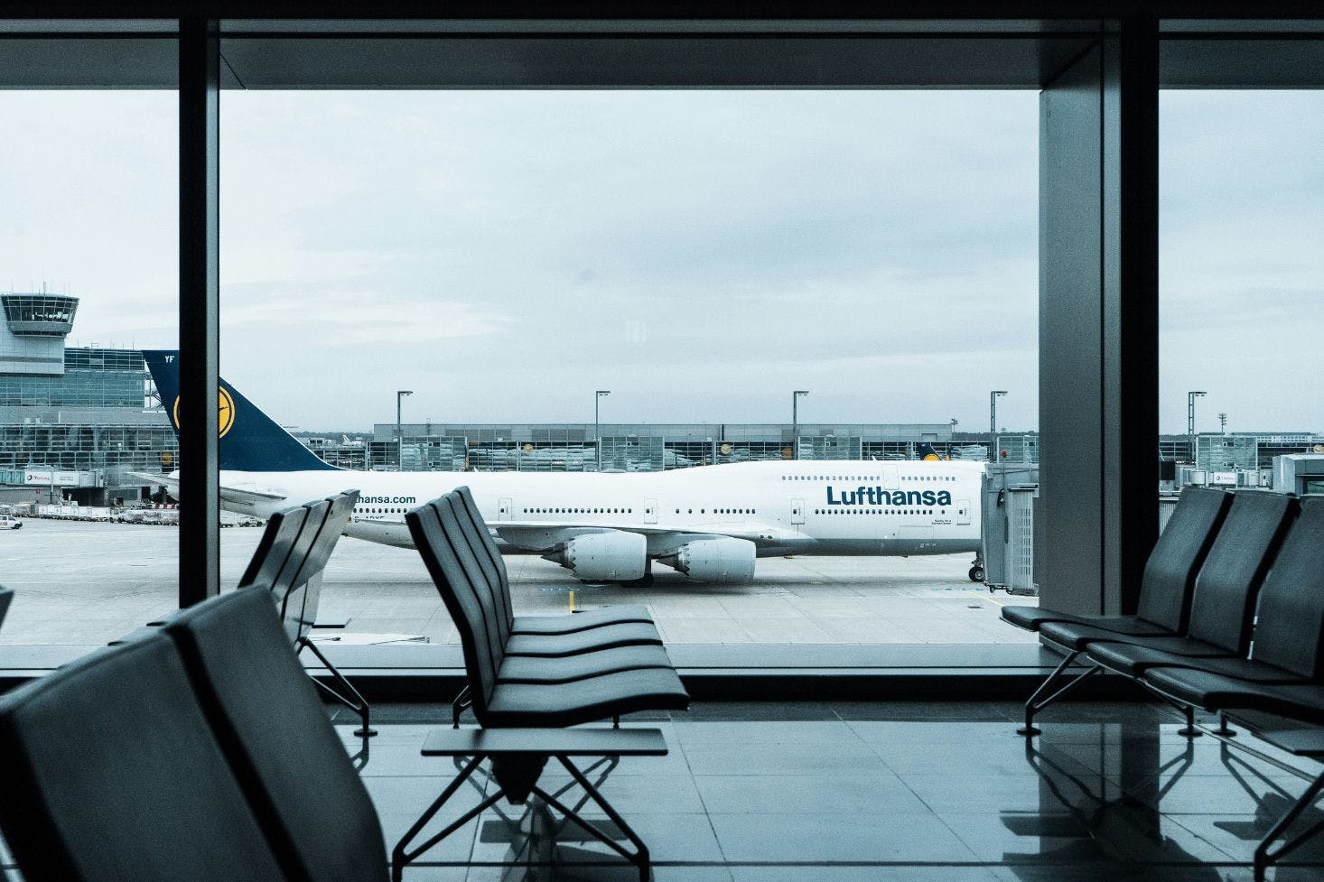 A Lufthansa plane parked at Frankfurt Airport, viewed through large terminal windows with empty seats inside