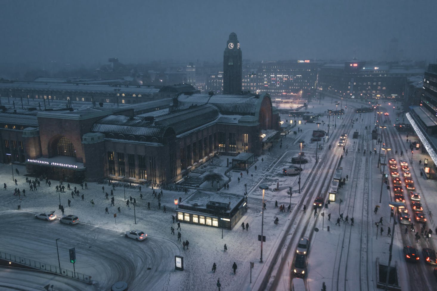 Vista dall'alto su Helsinki innevata a sera, con luci della città e viavai di auto e persone