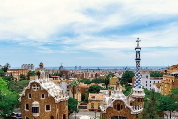 A view of colorful, Gaudí-style houses in Park Güell, Barcelona, with the city's sprawling skyline in the background