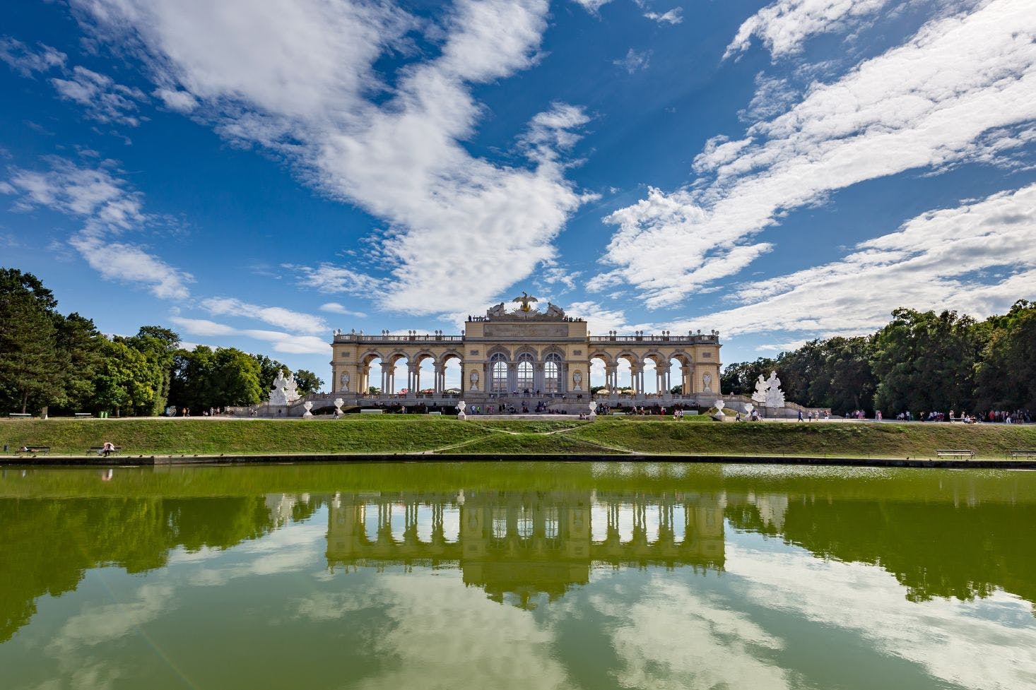 A view of Schönbrunn Palace in Vienna on a clear day, with its reflection glimmering in the lake in front