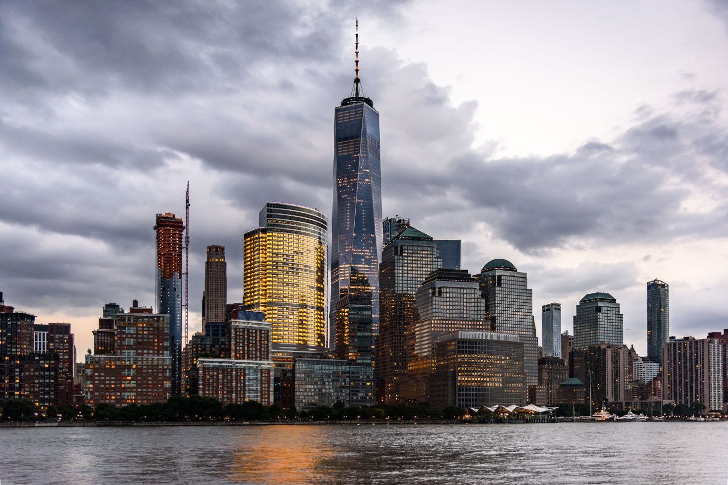 A view of New York City’s skyline with the One World Trade Center, reflecting lights under a cloudy sky