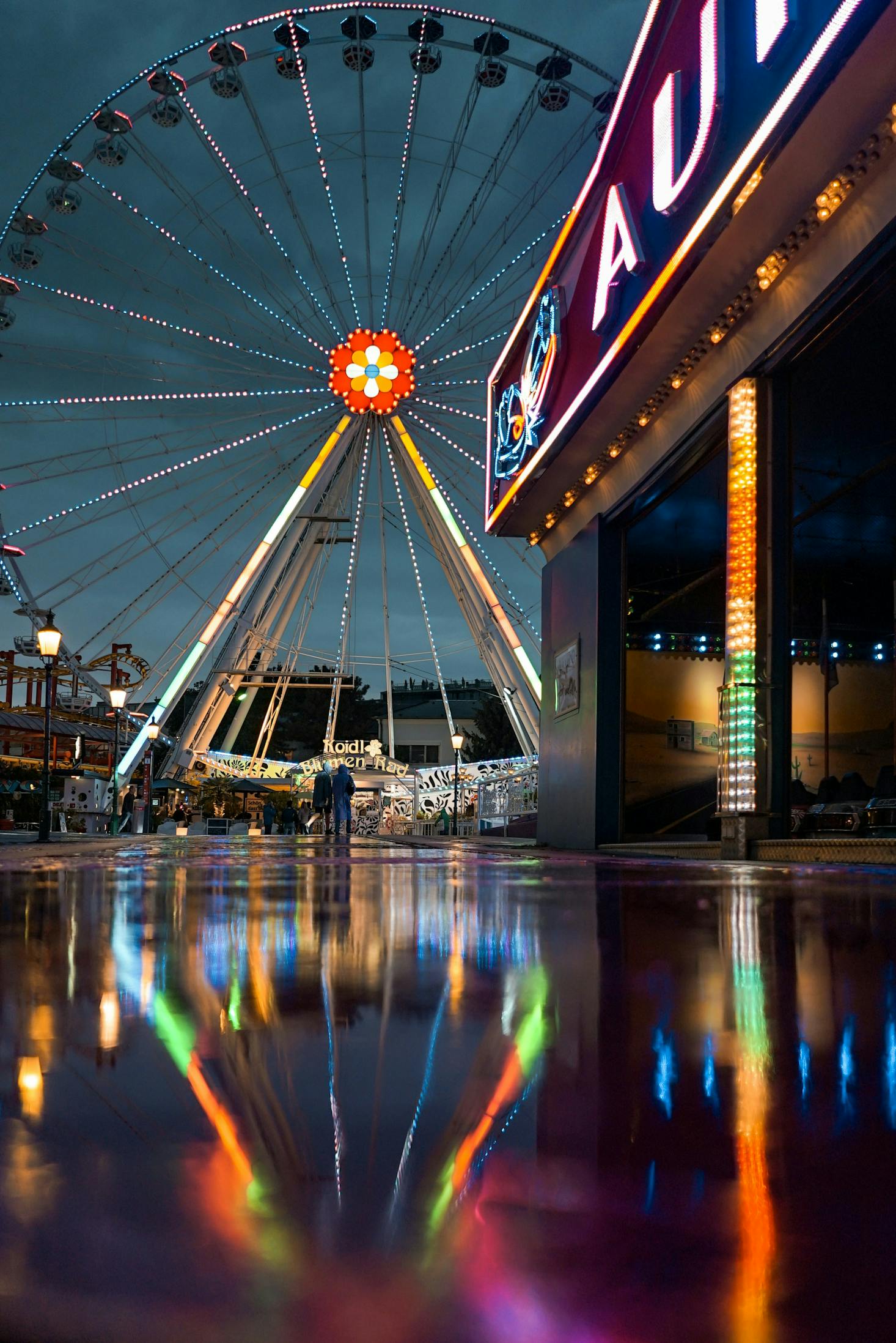 Giant Ferris wheel with bright neon lights reflected in a puddle at the Prater in Vienna at night