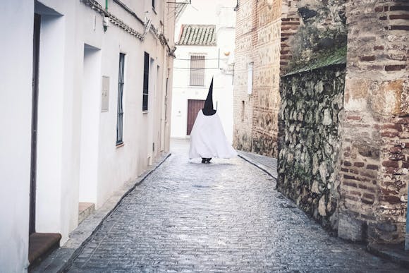 Semana Santa participant dressed in a traditional holy costume walking down a narrow alley way in Seville