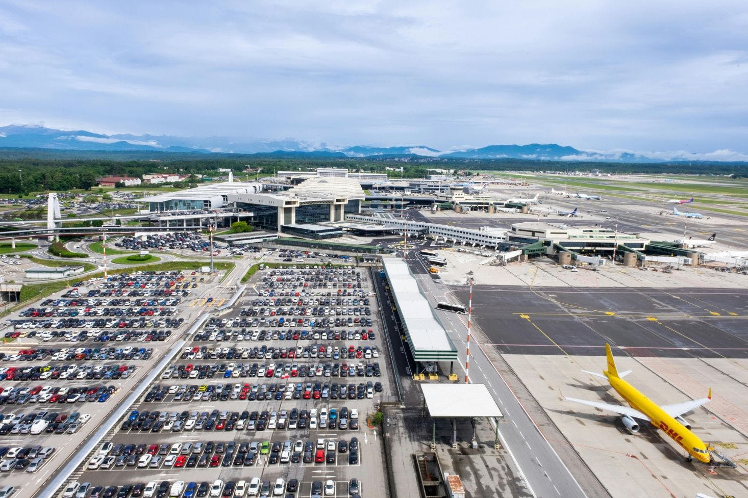 A view of Milano Malpensa Airport, a crowded parking lot, and a DHL plane on the tarmac