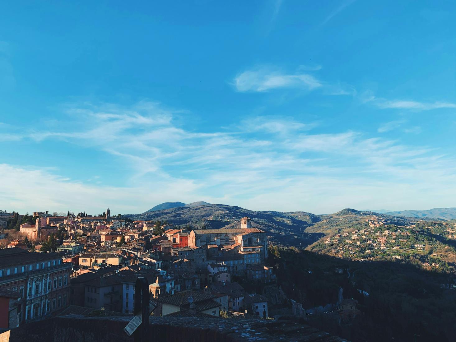 Città di Perugia dall'alto, con tetti degli edifici, montagne sullo sfondo e cielo azzurro