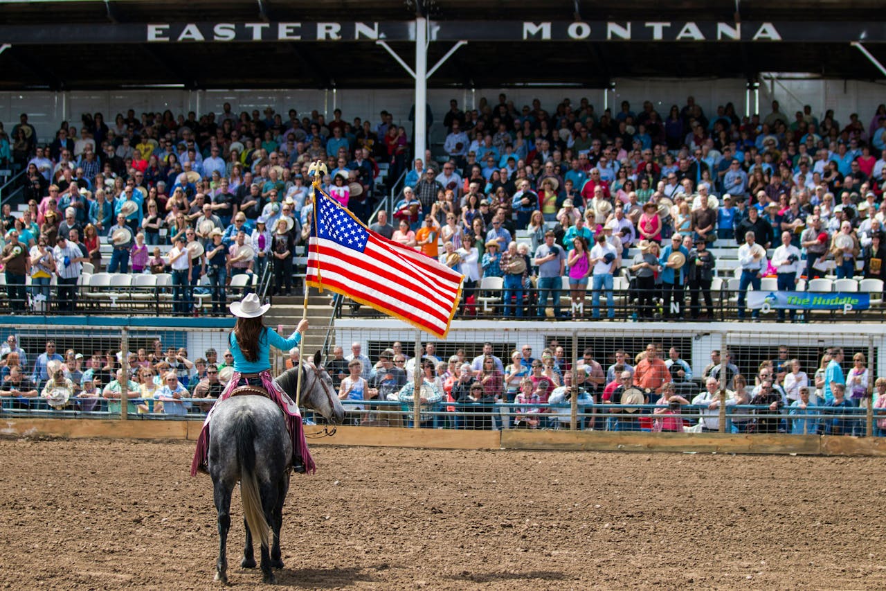 Woman riding a white horse and holding the US flag, presenting proudly in front of an audience