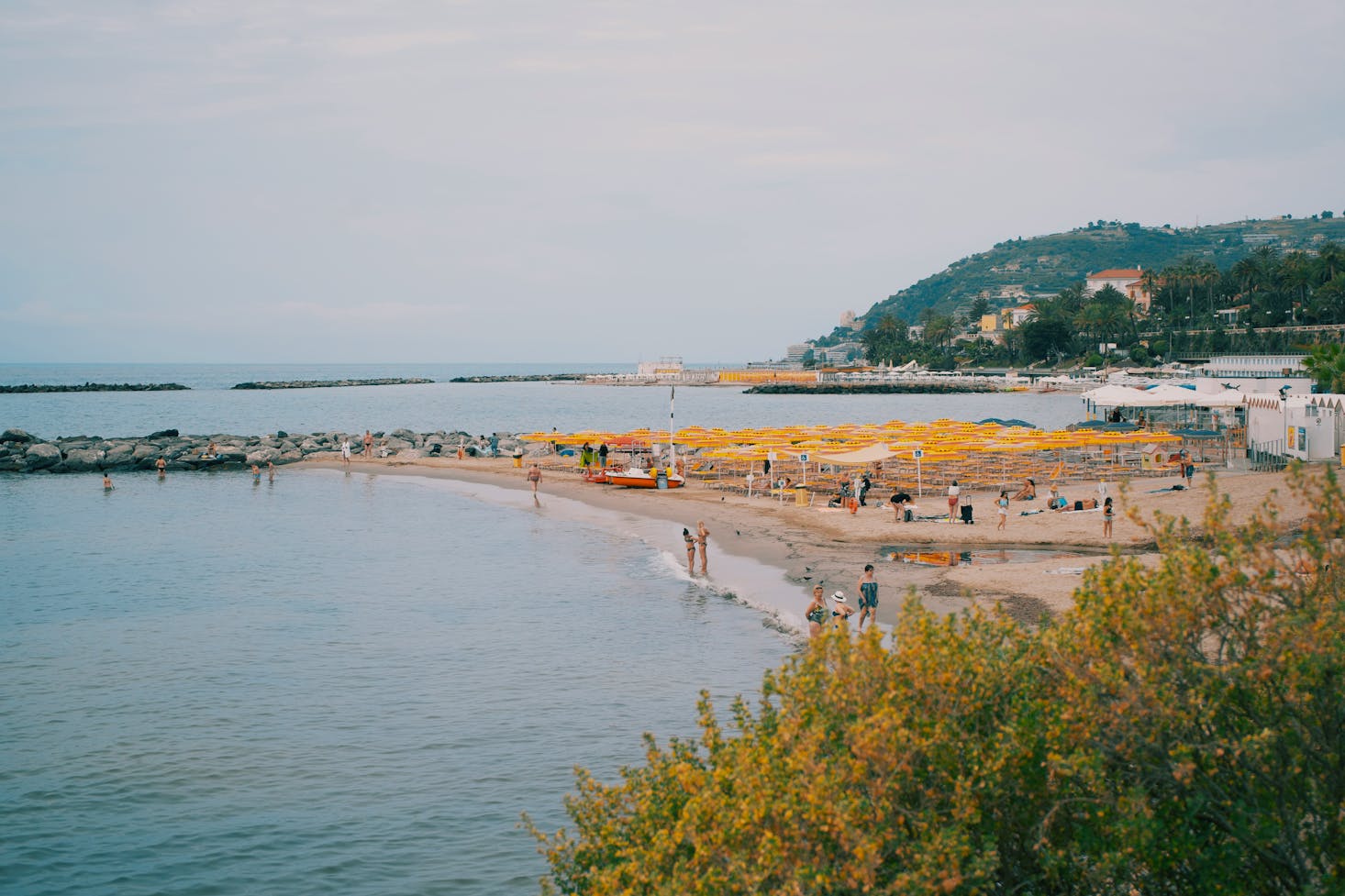 Bagnanti in spiaggia a Sanremo, mare sulla sinistra e area verde sulla destra