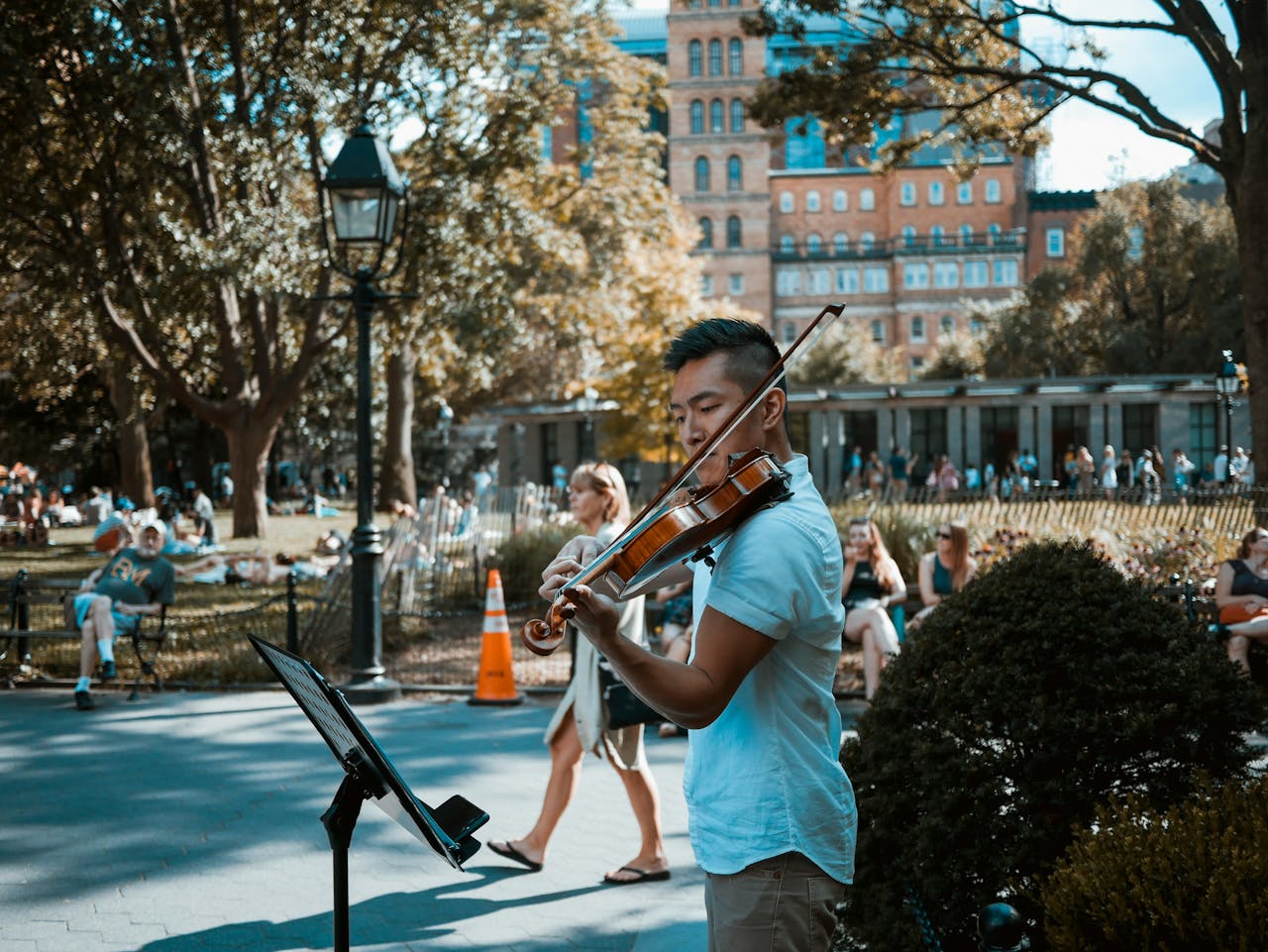 Street performer playing violin in a park as people gather to listen, capturing the outdoor charm of Adelaide Fringe