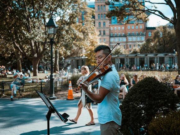 Street performer playing violin in a park as people gather to listen, capturing the outdoor charm of Adelaide Fringe