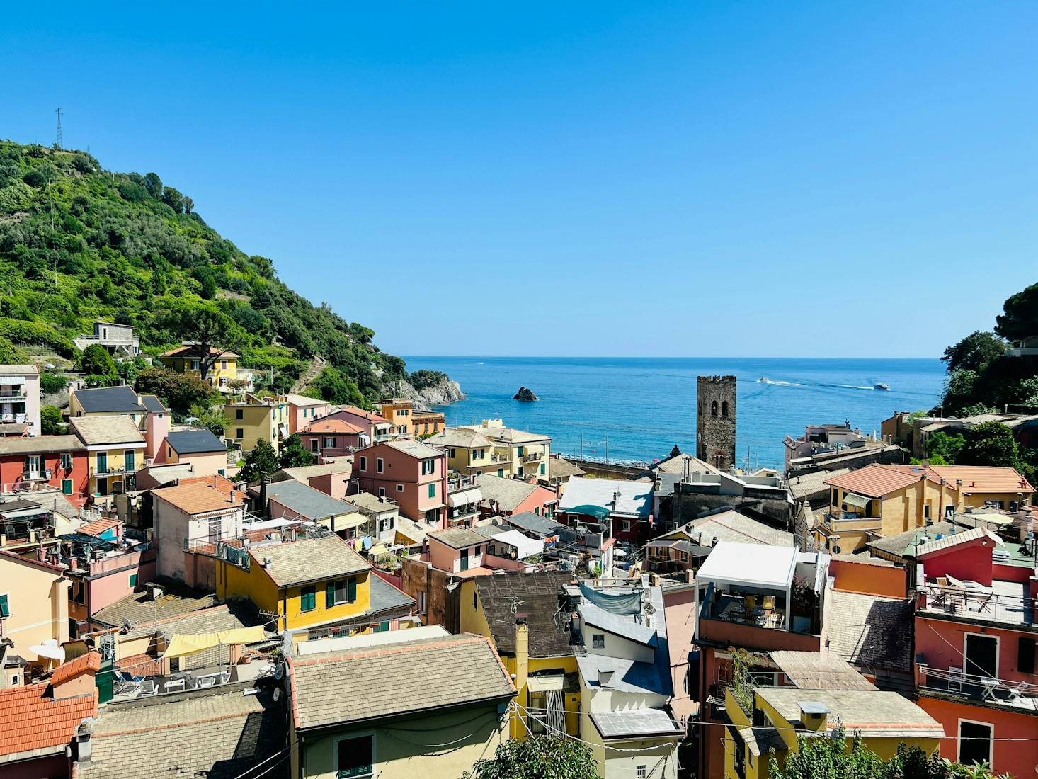 Vista dall'alto sui tetti di Monterosso, con alture verdi a sinistra e mare sullo sfondo