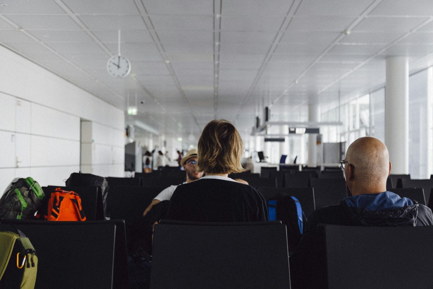 Three passengers with backpacks sitting in the white hall of Munich Airport