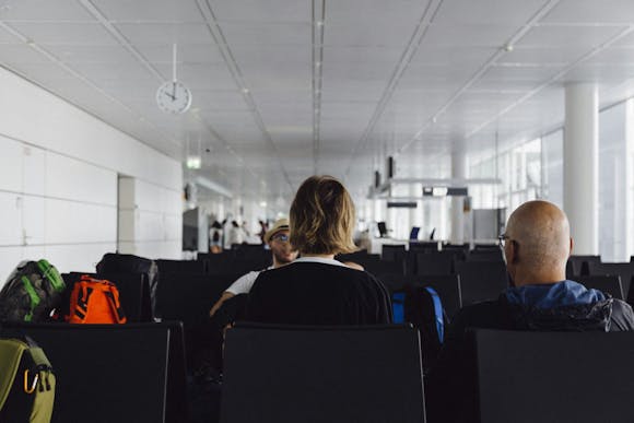 Three passengers with backpacks sitting in the white hall of Munich Airport