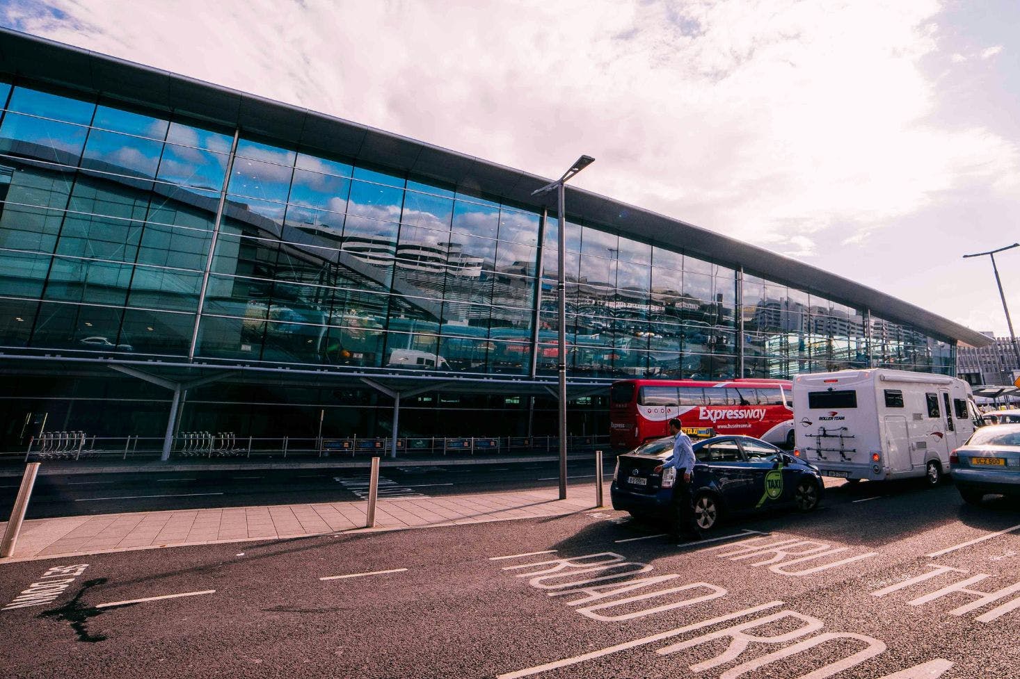 Front of the Dublin Airport glass building with two buses, and two taxis waiting in front of it