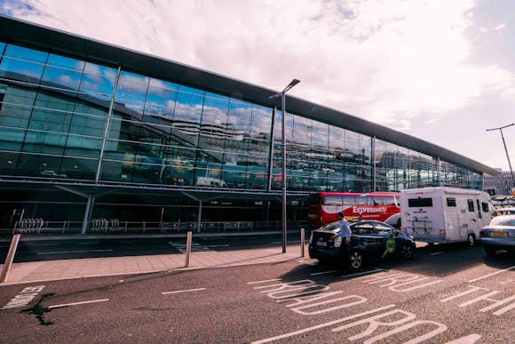 Front of the Dublin Airport glass building with two buses, and two taxis waiting in front of it