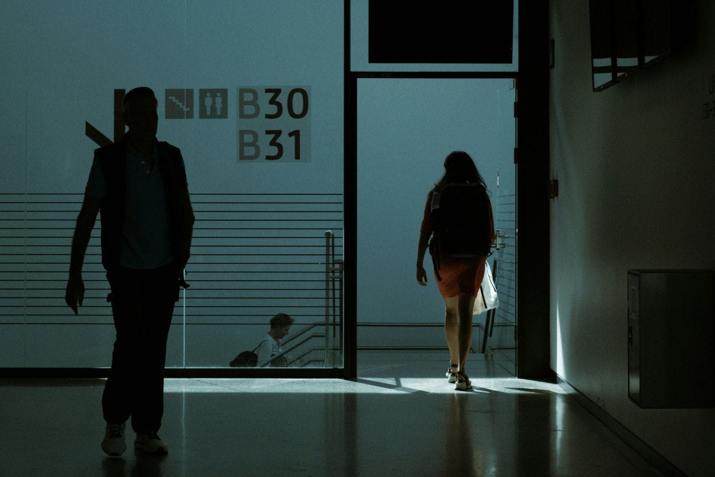 A woman and a man walking toward the staircase through the dark hallway of the Berlin Brandenburg Airport 