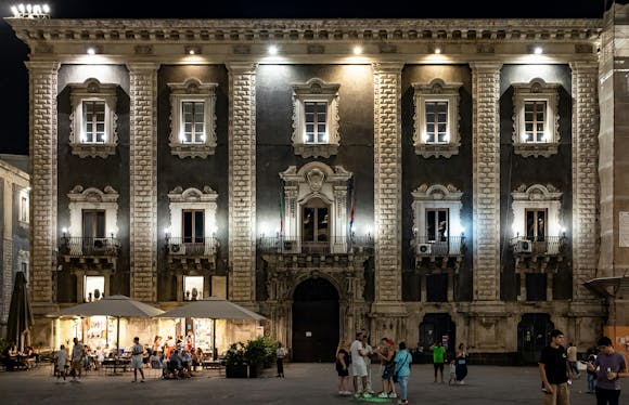 An ornate building in Catania's Old Town lit up at night with an outdoor restaurant