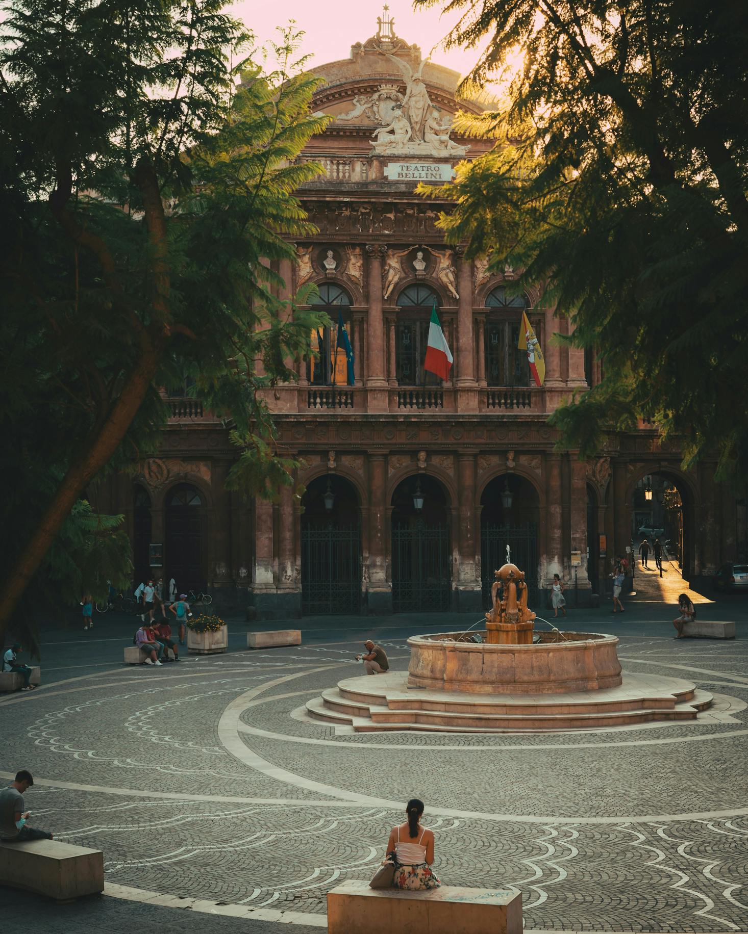 A fountain in a small square in front of an ornate historic building in Catania at sunset