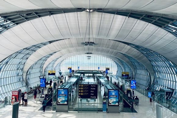 Oval-shaped glass hall at Suvarnabhumi Airport, Bangkok, with gates, signs, seating area, and passengers