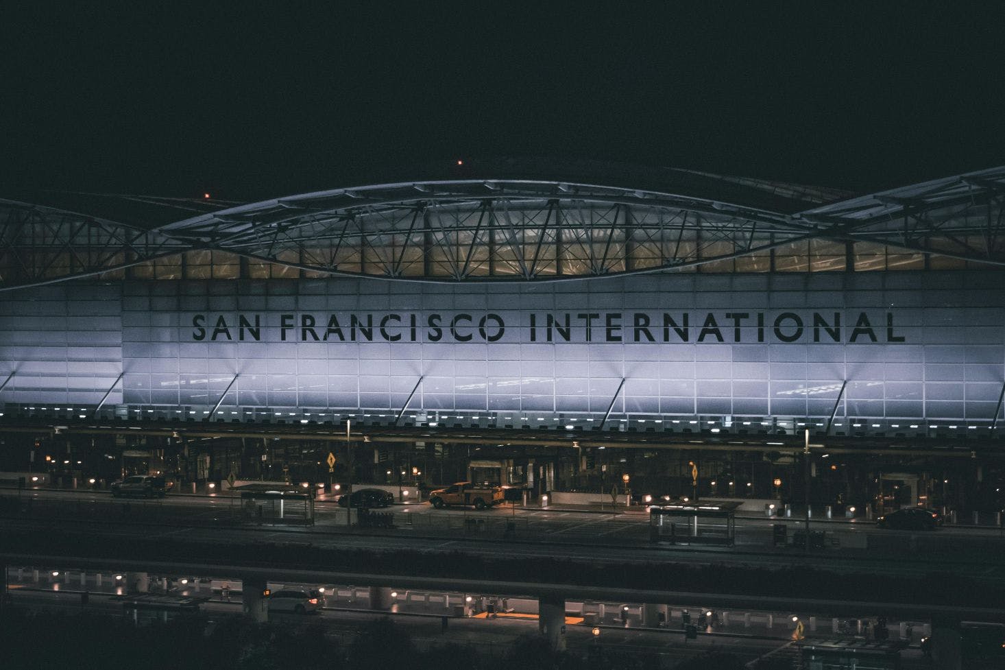 San Francisco International Airport lit up at night, with vehicles parked in front and in the underground parking area