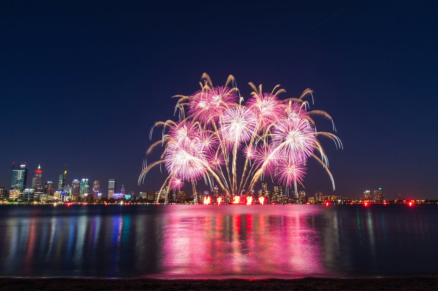 A pink fireworks show on the water in Perth at night