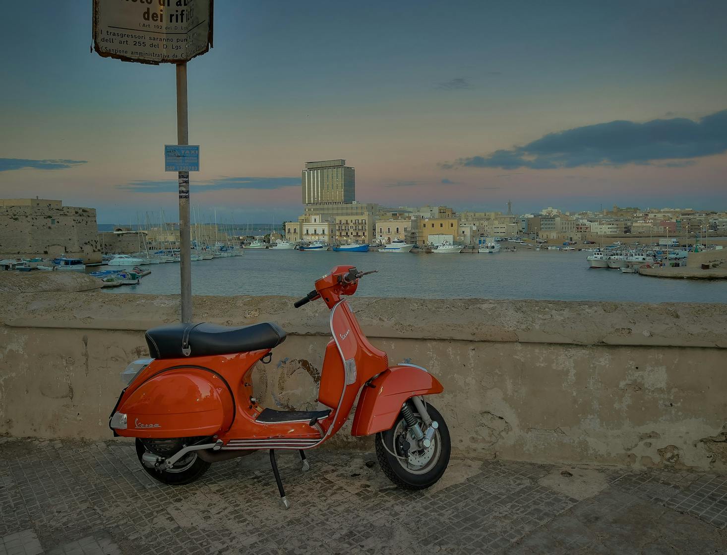 Lungomare di Gallipoli con edifici sullo sfondo e vespa rossa in primo piano