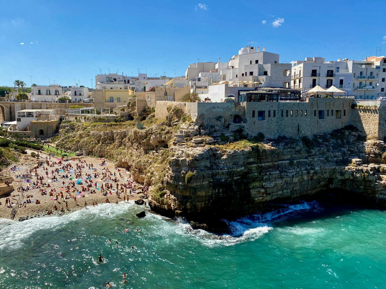 Cala Lama Monachile a Polignano a Mare, con bagnanti in spiaggia, celebre scogliera e acque cristalline