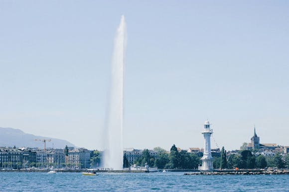 Geneva's Jet d'Eau fountain over Lake Geneva, with a lighthouse and city buildings in the background