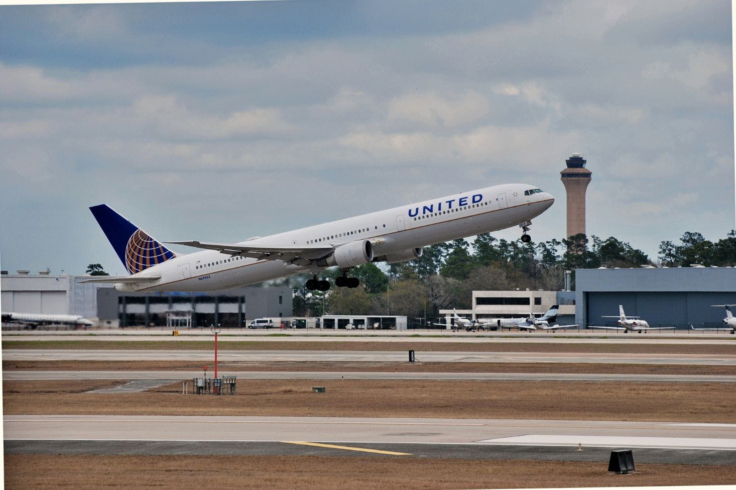 A plane takes off from Houston International Airport (IAH) with control tower and other short buildings in the background