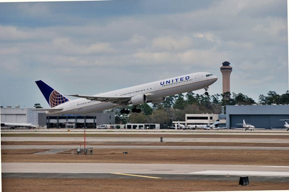 A plane takes off from Houston International Airport (IAH) with control tower and other short buildings in the background