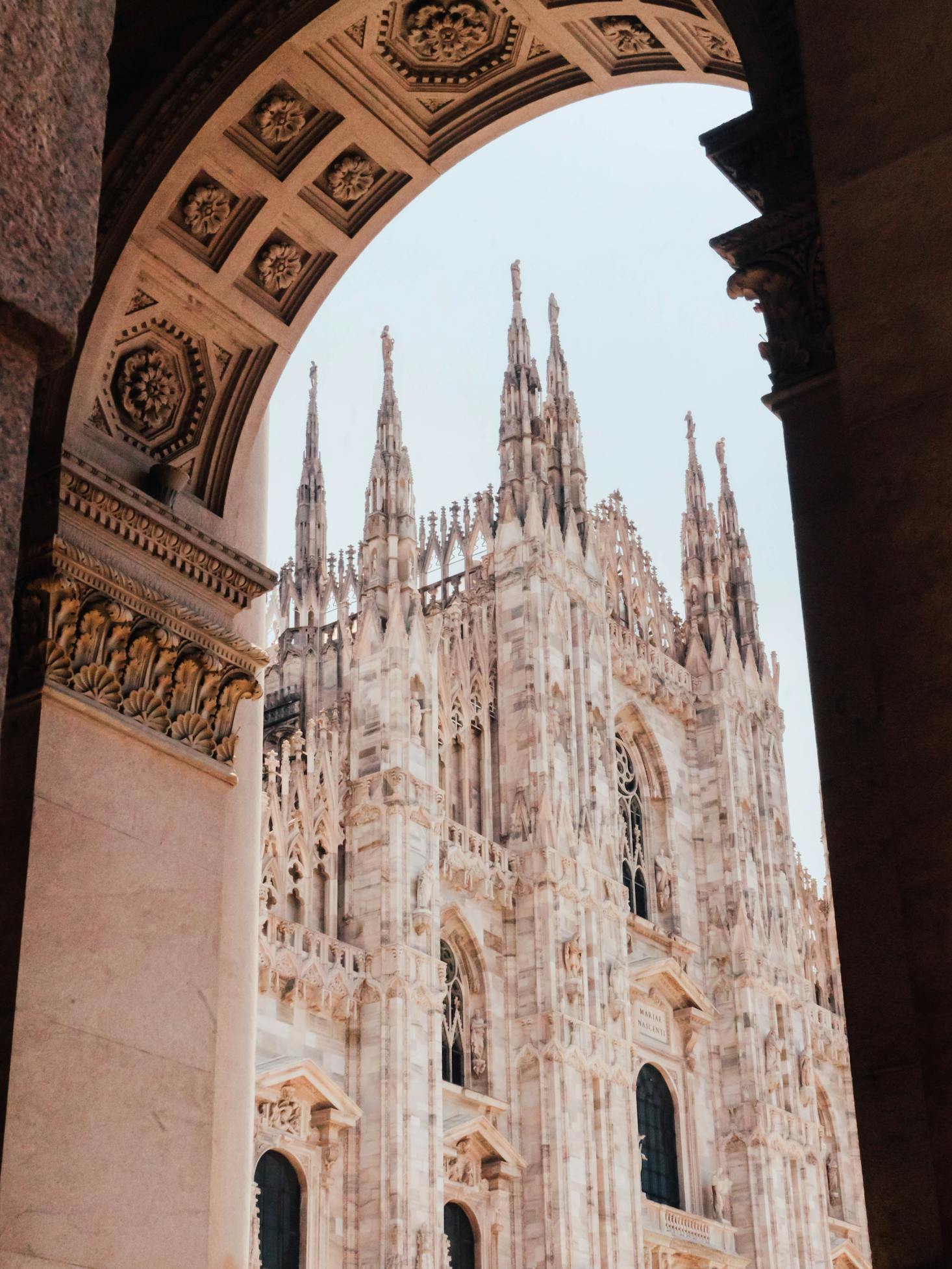 A view through an arch of the intricate white facade of Duomo Milan