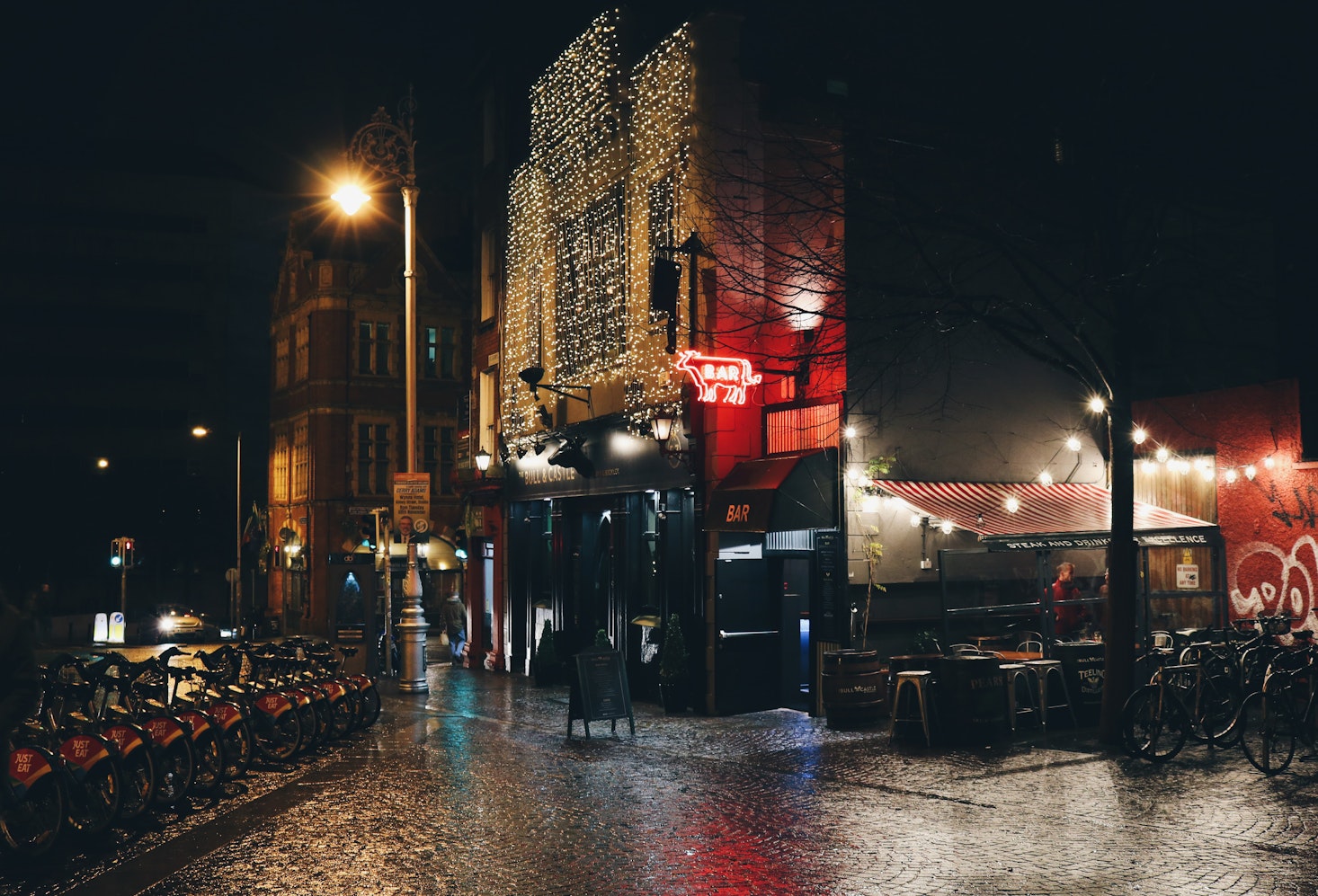 A Dublin bar illuminated with festive holiday lights at night, flanked by bike racks on both sides