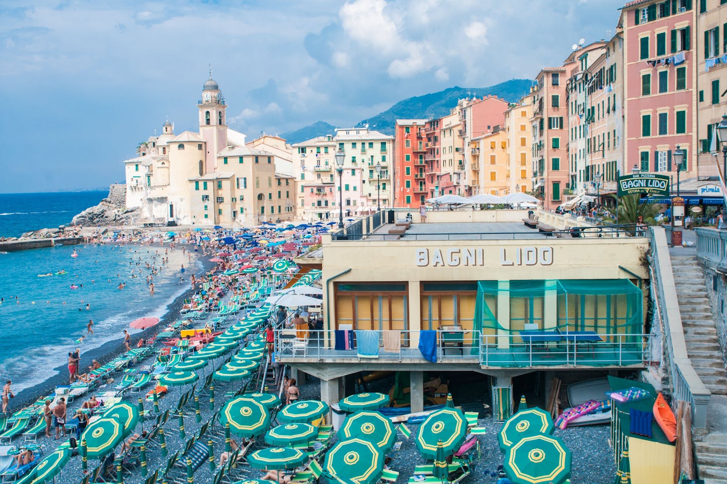 Genoa beach club with chairs set along the water and colorful buildings in the background