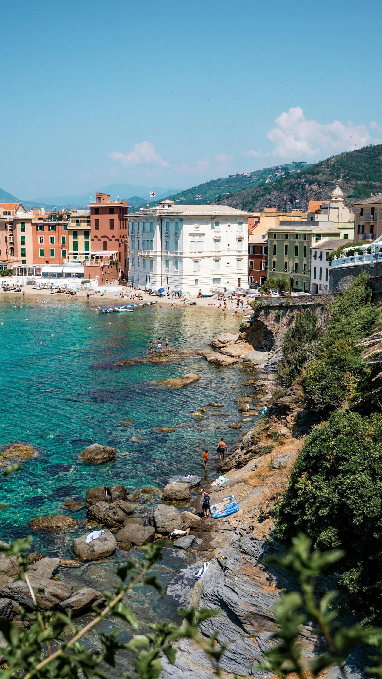 The coast of Genoa, Italy with a rocky beach area flanked by buildings and a backdrop of mountains